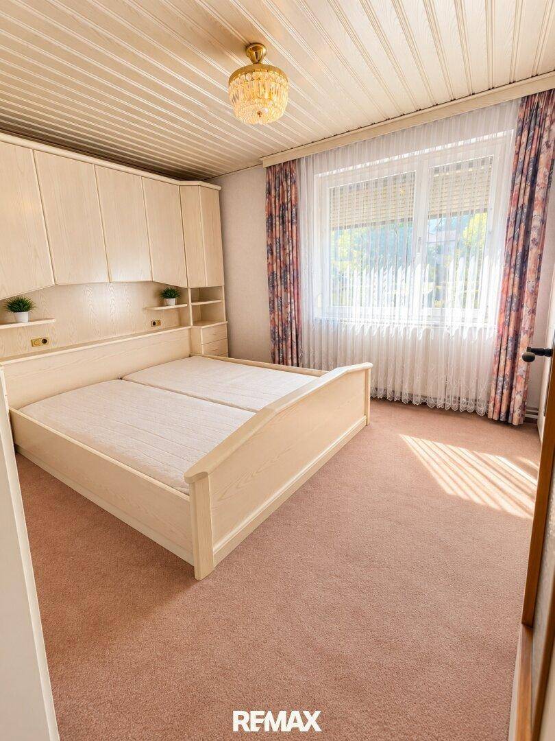 Schlafzimmer mit Doppelbett, Einbauschränken und Teppichboden, hell durch großes Fenster.