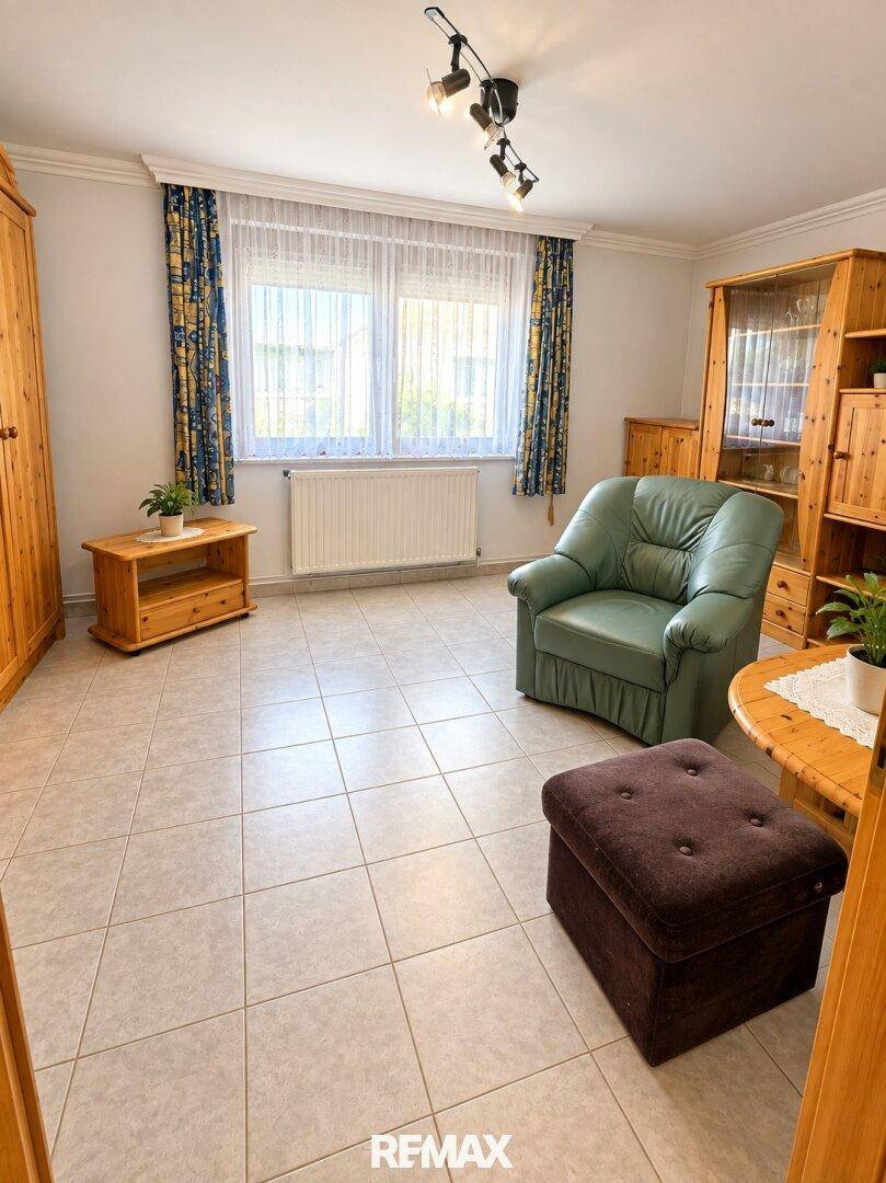 Wohnzimmer mit hellgrauen Fliesen, Holzmöbeln und einem bequemen grünen Sessel.