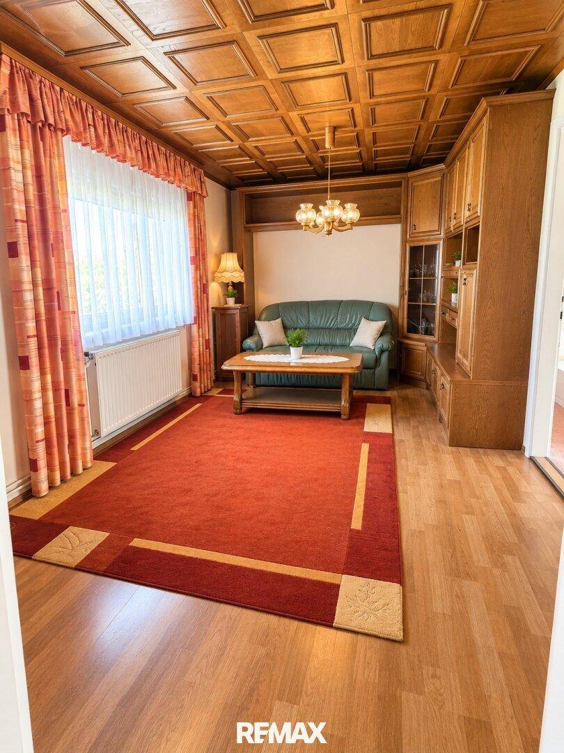 Gemütliches Wohnzimmer mit Holzdecke, Holzmöbeln und einem großen roten Teppich.