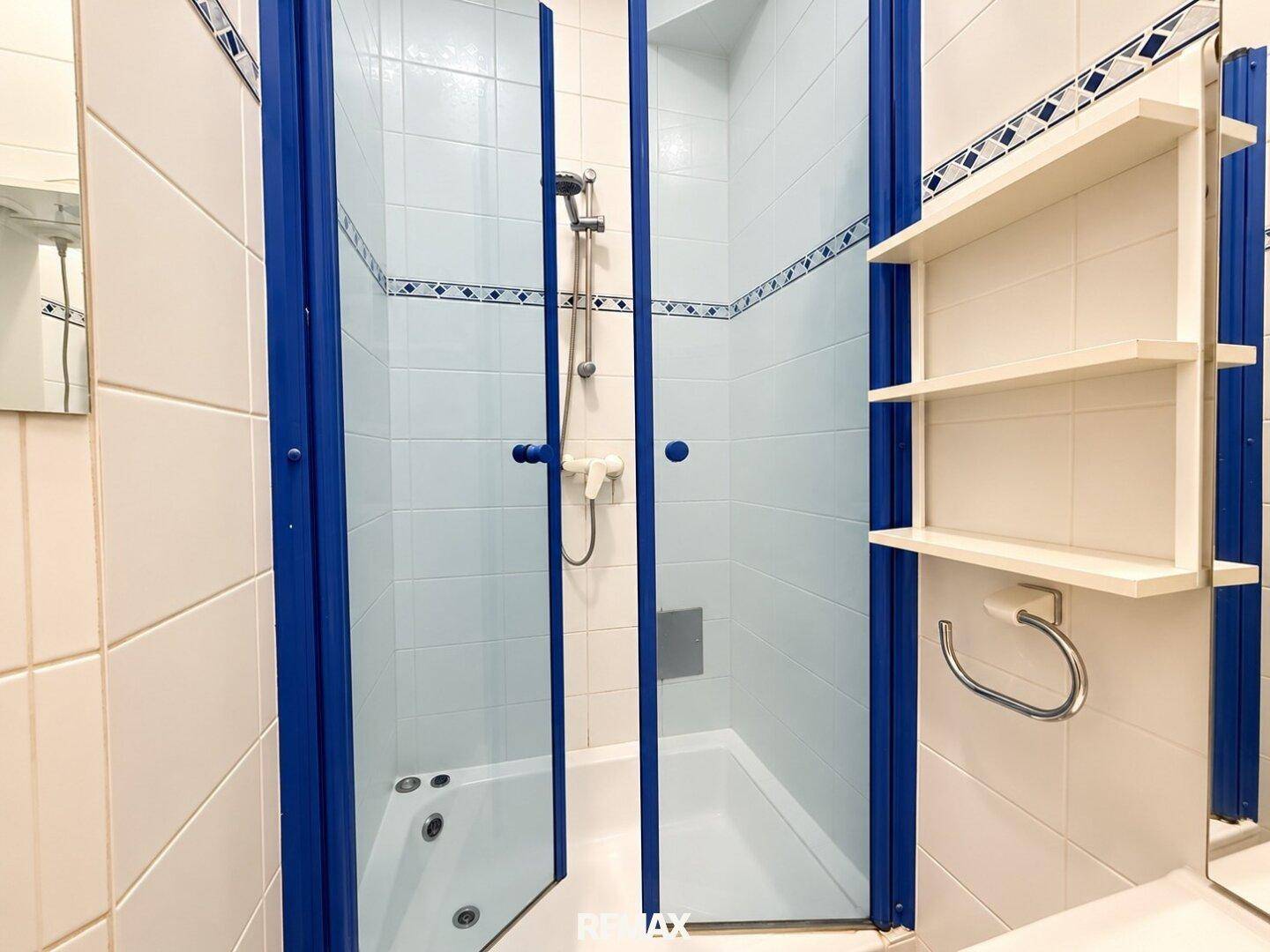 Badezimmer mit Duschkabine, blauen Akzenten und weißen Fliesen, funktional und hell.