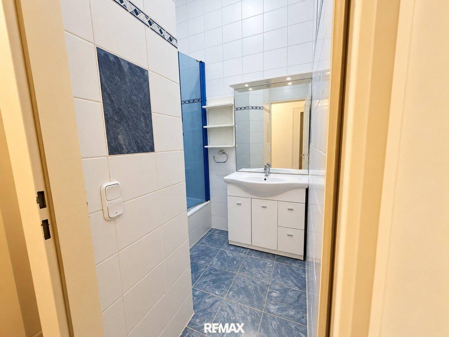 Badezimmer mit Waschbecken, Spiegel und blauen Fliesen, bietet grundlegende Ausstattung.