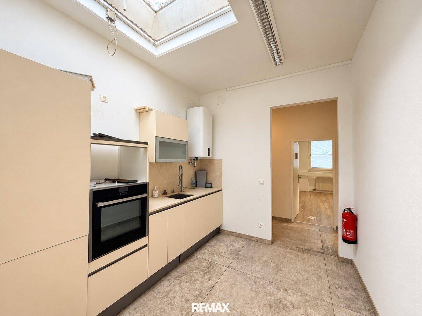 Kleine Küchenzeile mit beigen Schränken, Spüle und Backofen, beleuchtet durch ein Oberlicht in der Decke.
