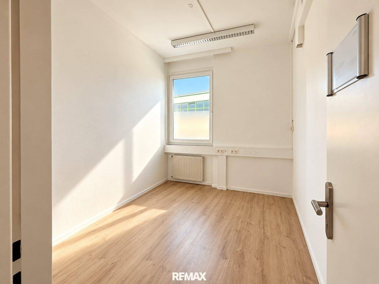Kleines, helles Büro mit Laminatboden, weißen Wänden und einem Fenster mit Sichtschutzfolie.