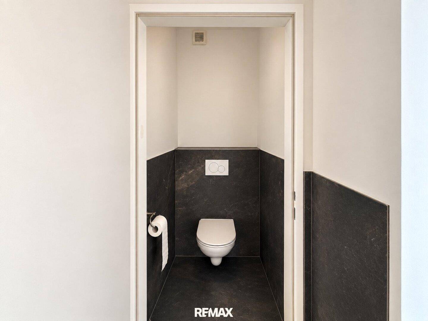 Modernes WC mit wandhängender Toilette und dunklen Fliesen an den Wänden, in einem minimalistischen Design.