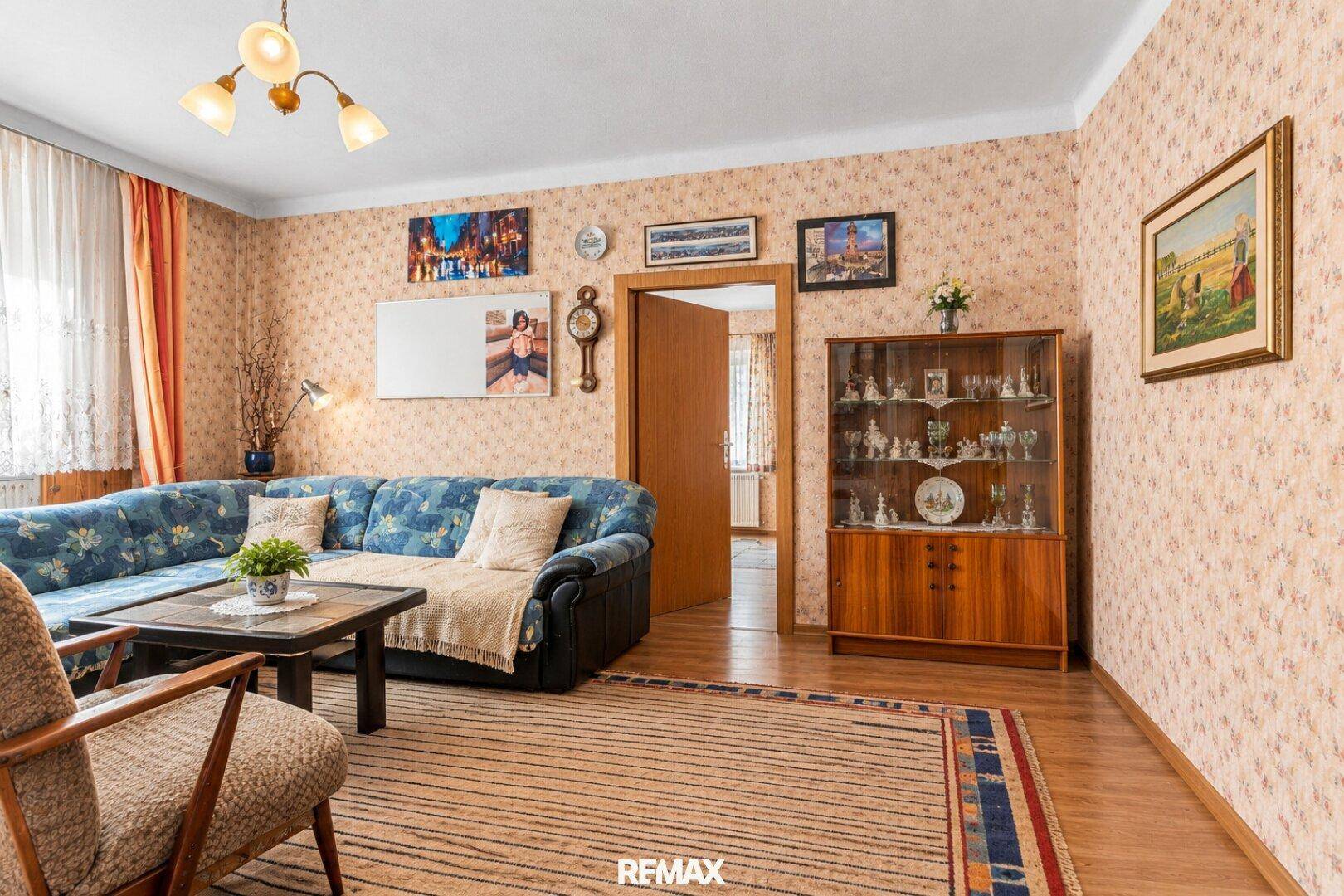 Geräumiges Wohnzimmer mit bequemer Couch, Holzmöbeln und gemusterter Tapete.