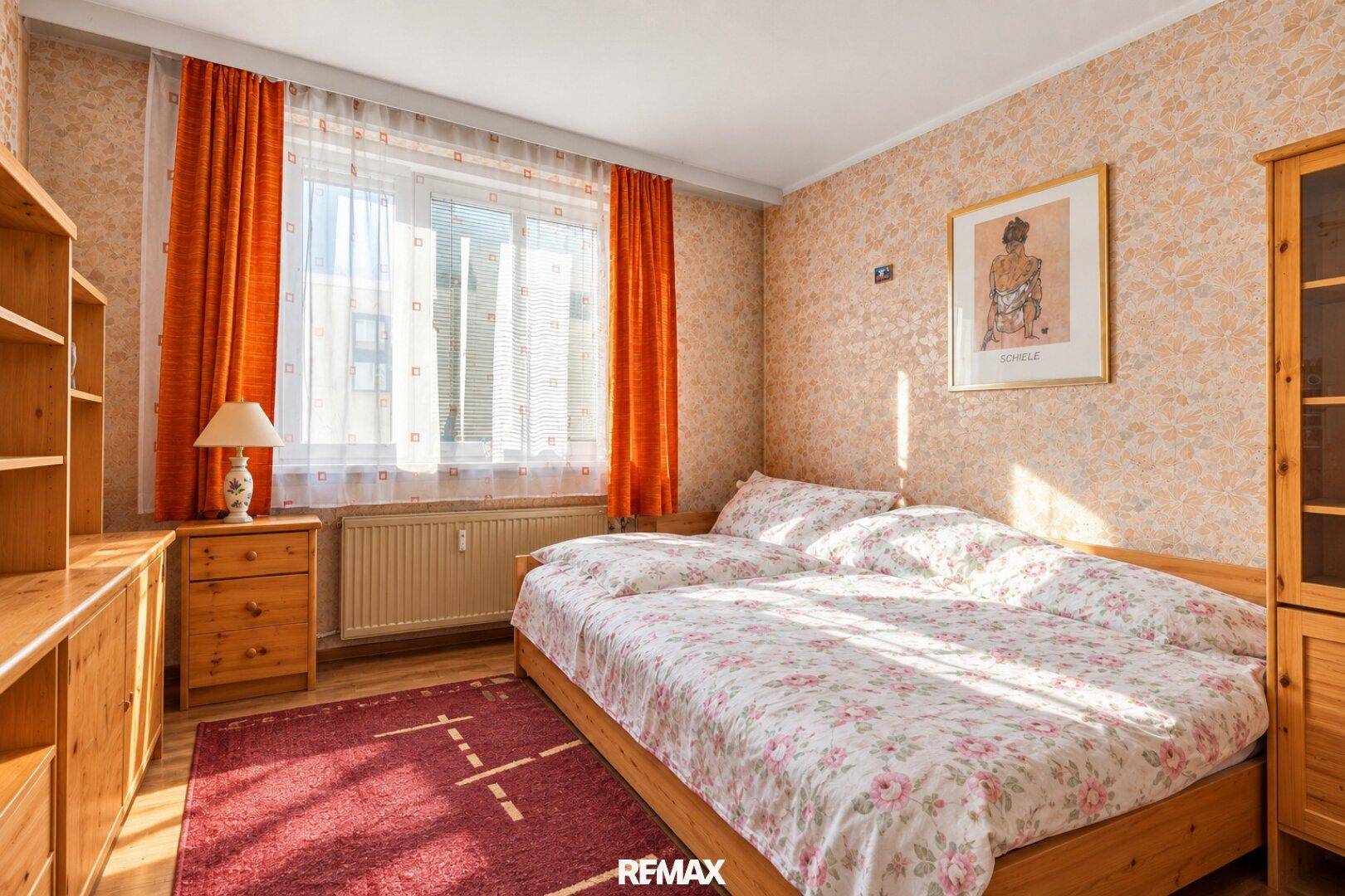 Helles Schlafzimmer mit Doppelbett, Holzmöbeln und gemusterter Tapete.