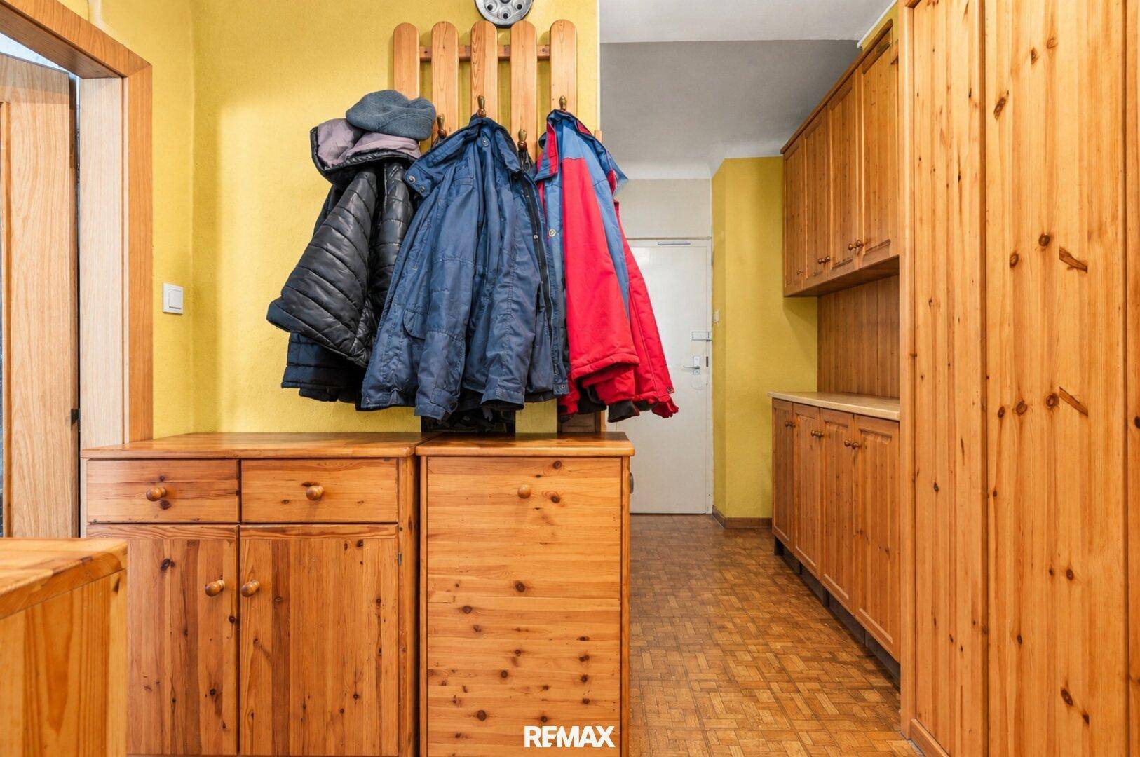 Heller Eingangsbereich mit gelben Wänden, Holzmöbeln und Garderobe.