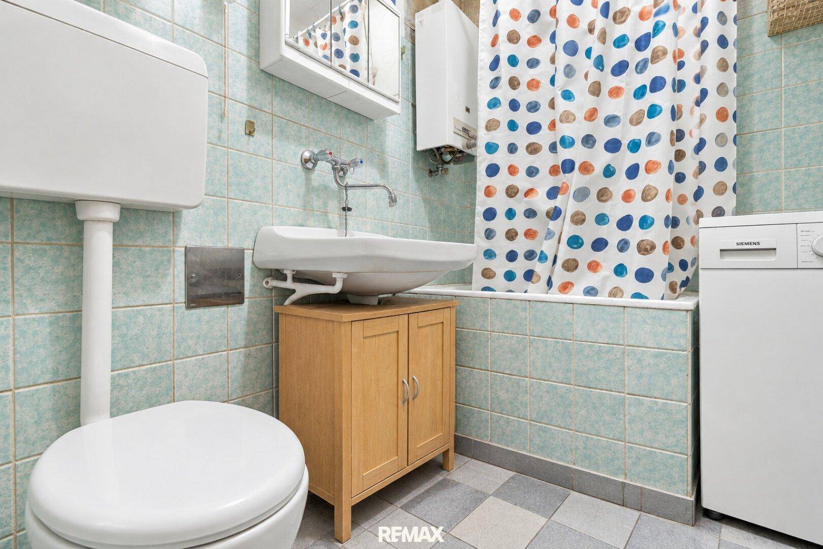 Badezimmer mit Badewanne, WC, Waschbecken und hellblauen Fliesen.
