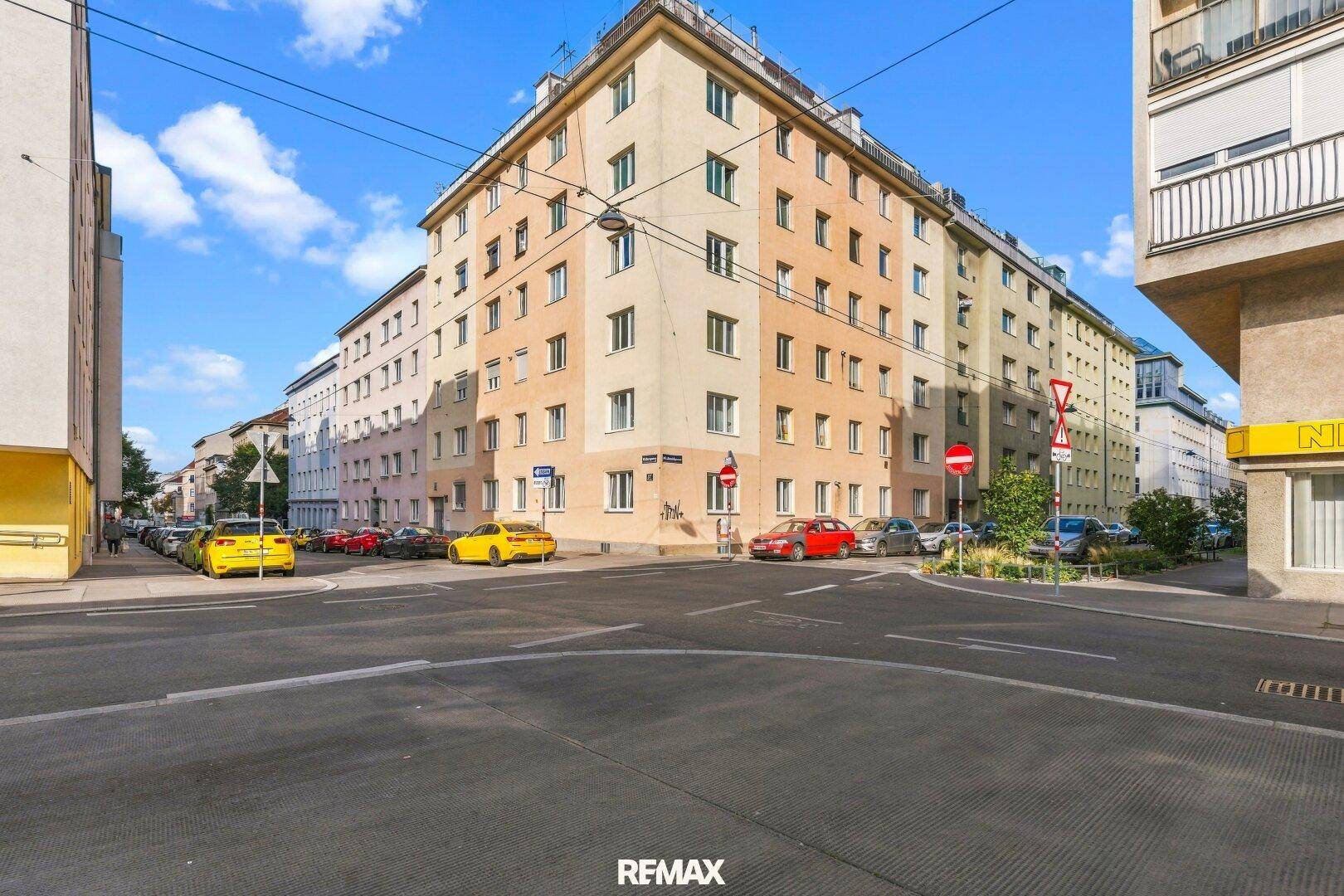 Mehrstöckiges Wohngebäude an einer Straßenecke mit parkenden Autos.