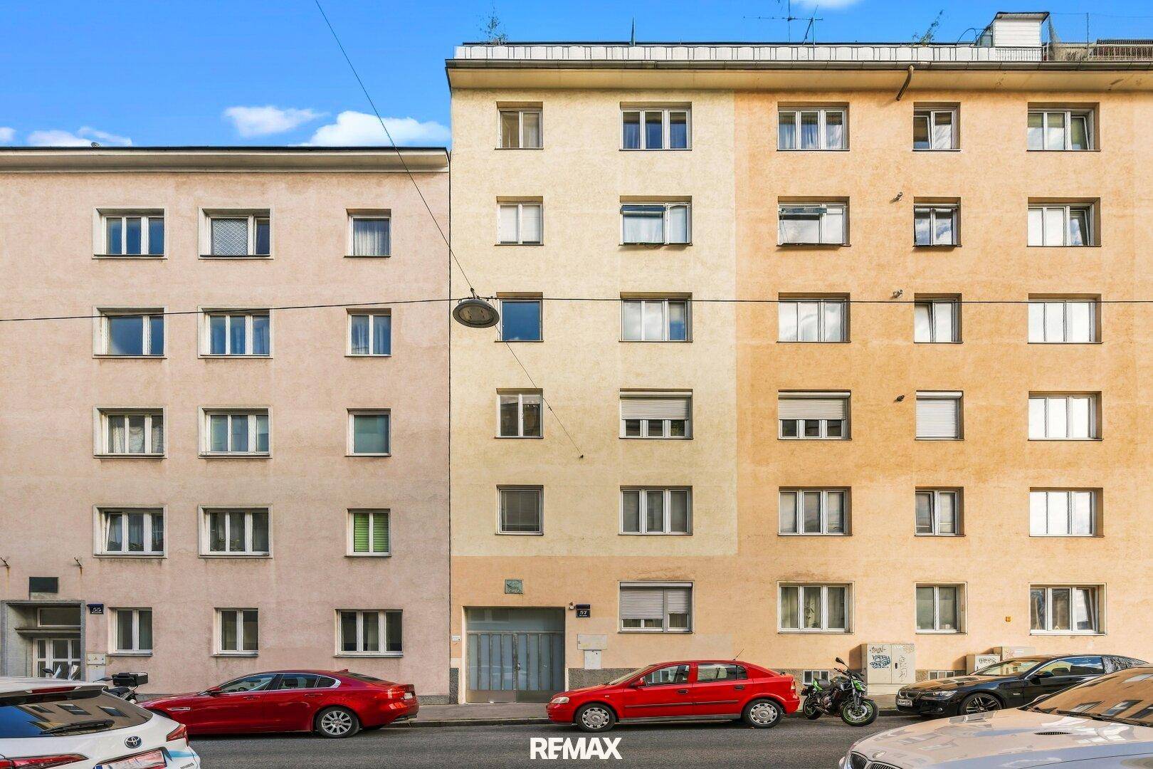 Fassade eines mehrstöckigen Wohnhauses mit vielen Fenstern und geparkten Autos.