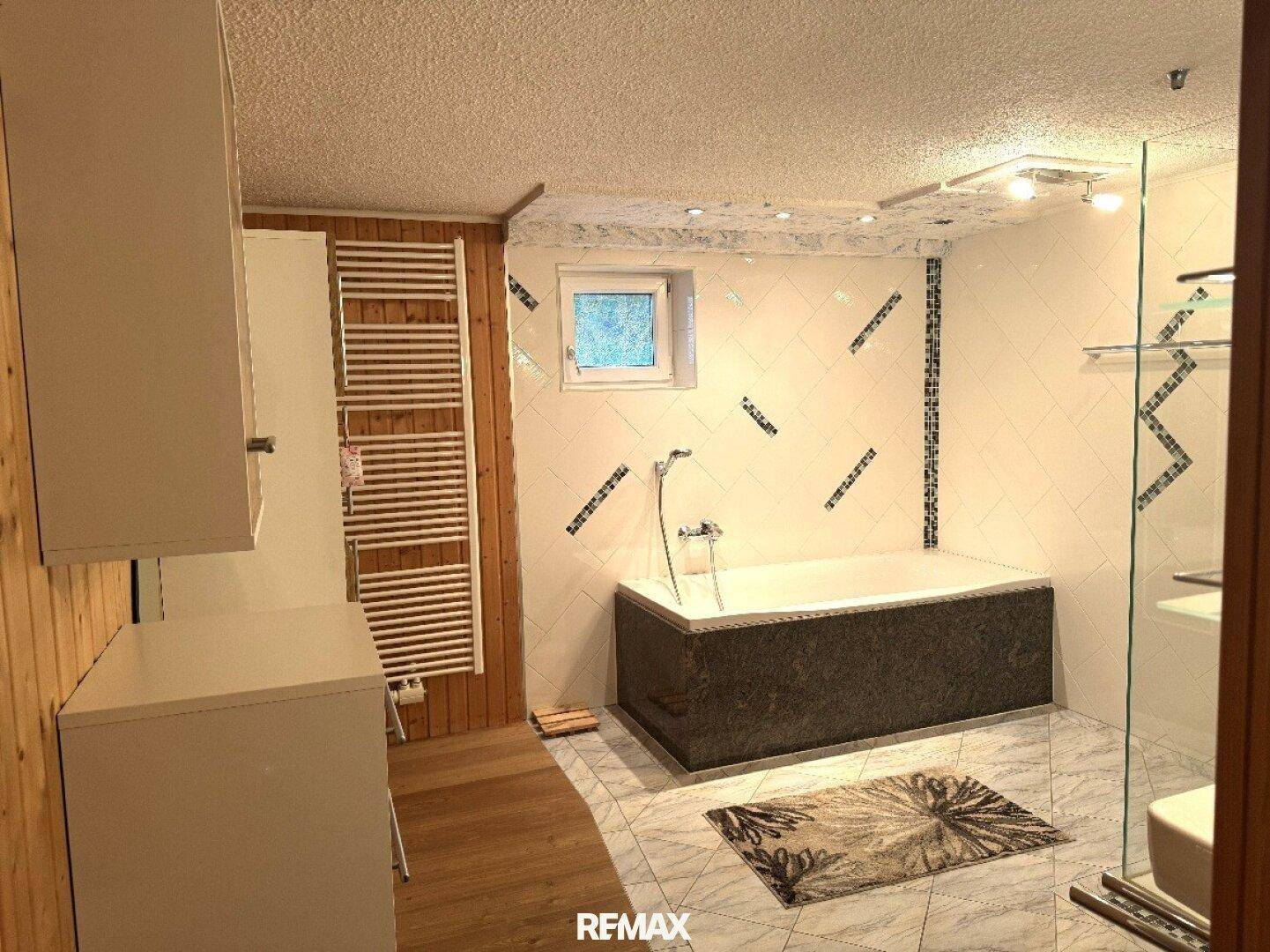 Badezimmer mit Badewanne, Duschbereich und Holzwänden, kombiniert mit modernen Fliesen.