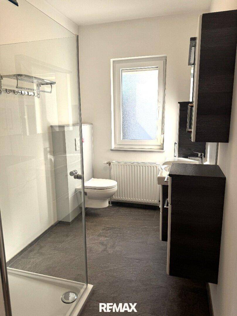 Modernes Badezimmer mit ebenerdiger Dusche, WC und dunklem Waschtischunterschrank.