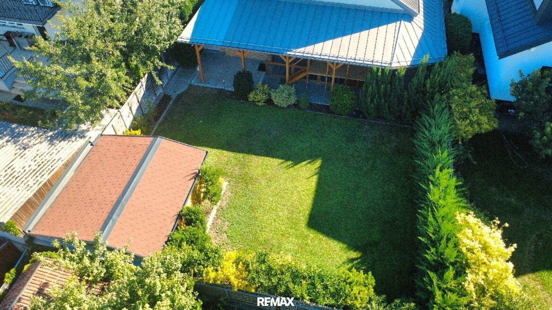 Gepflegter Gartenbereich mit Rasenfläche, Gartenhaus und überdachtem Terrassenbereich.