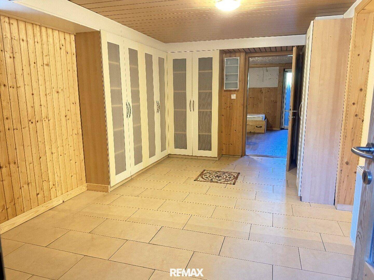 Schlafzimmer mit Einbauschränken, Fliesenboden und Holzdeckenverkleidung.