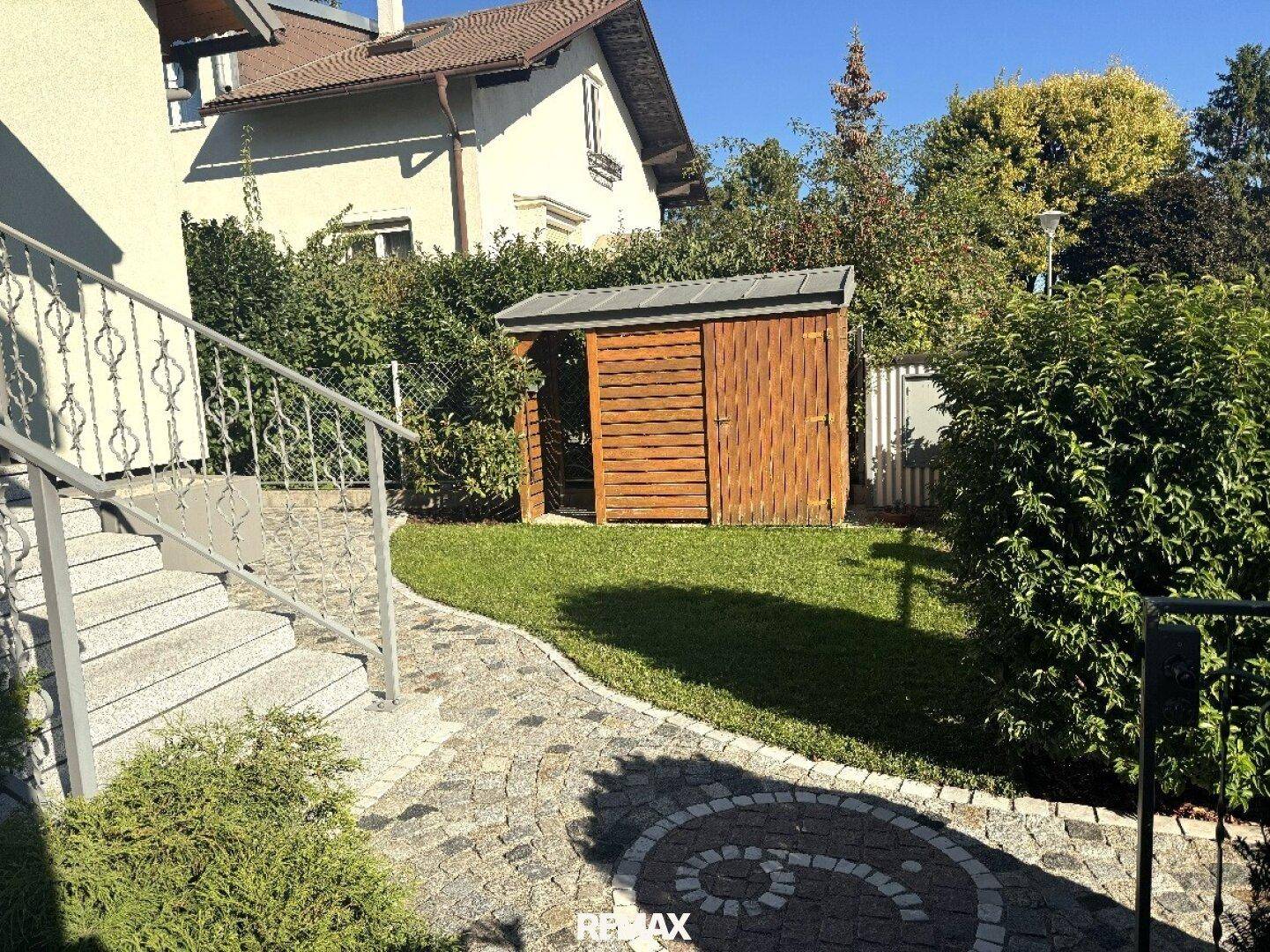 Gepflegter Gartenbereich mit Rasen, Steintreppe und einem kleinen Gartenhaus.