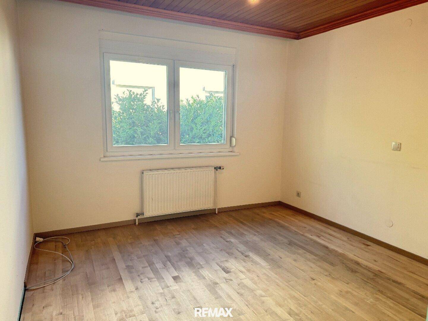 Helles Zimmer mit Holzfußboden, Fenster und Heizkörper, bereit zur individuellen Gestaltung.