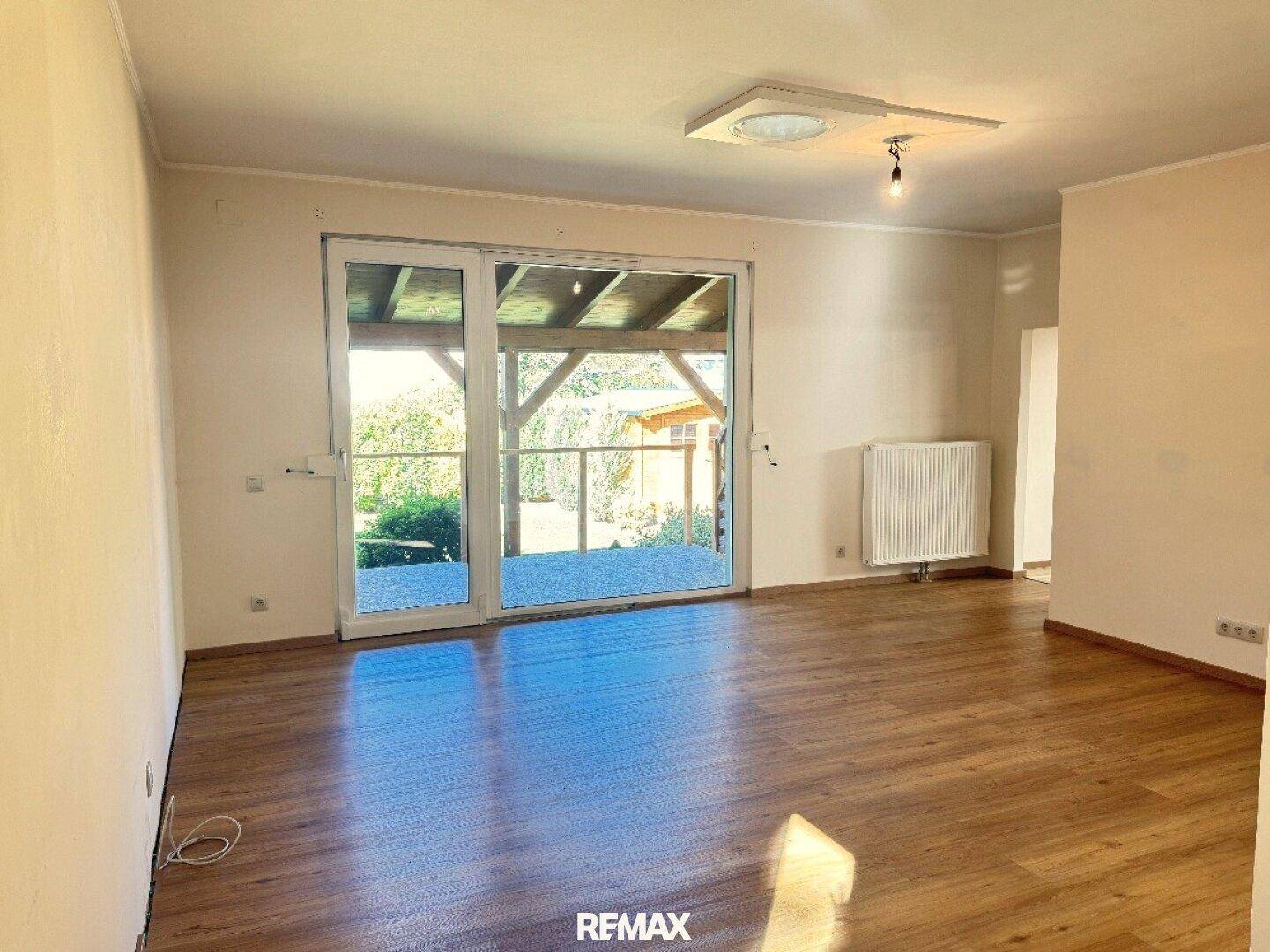 Helles Wohnzimmer mit Laminatboden und großzügigem Zugang zu einer überdachten Terrasse.