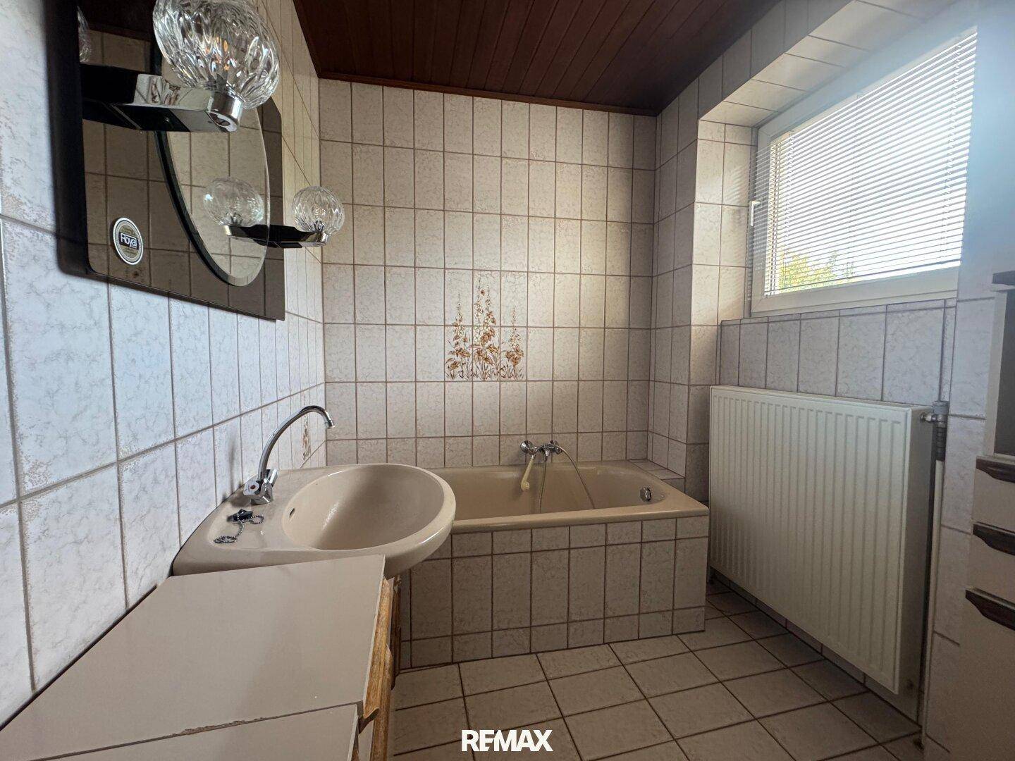 Badezimmer mit Fliesen, Badewanne, Waschbecken und Fenster.