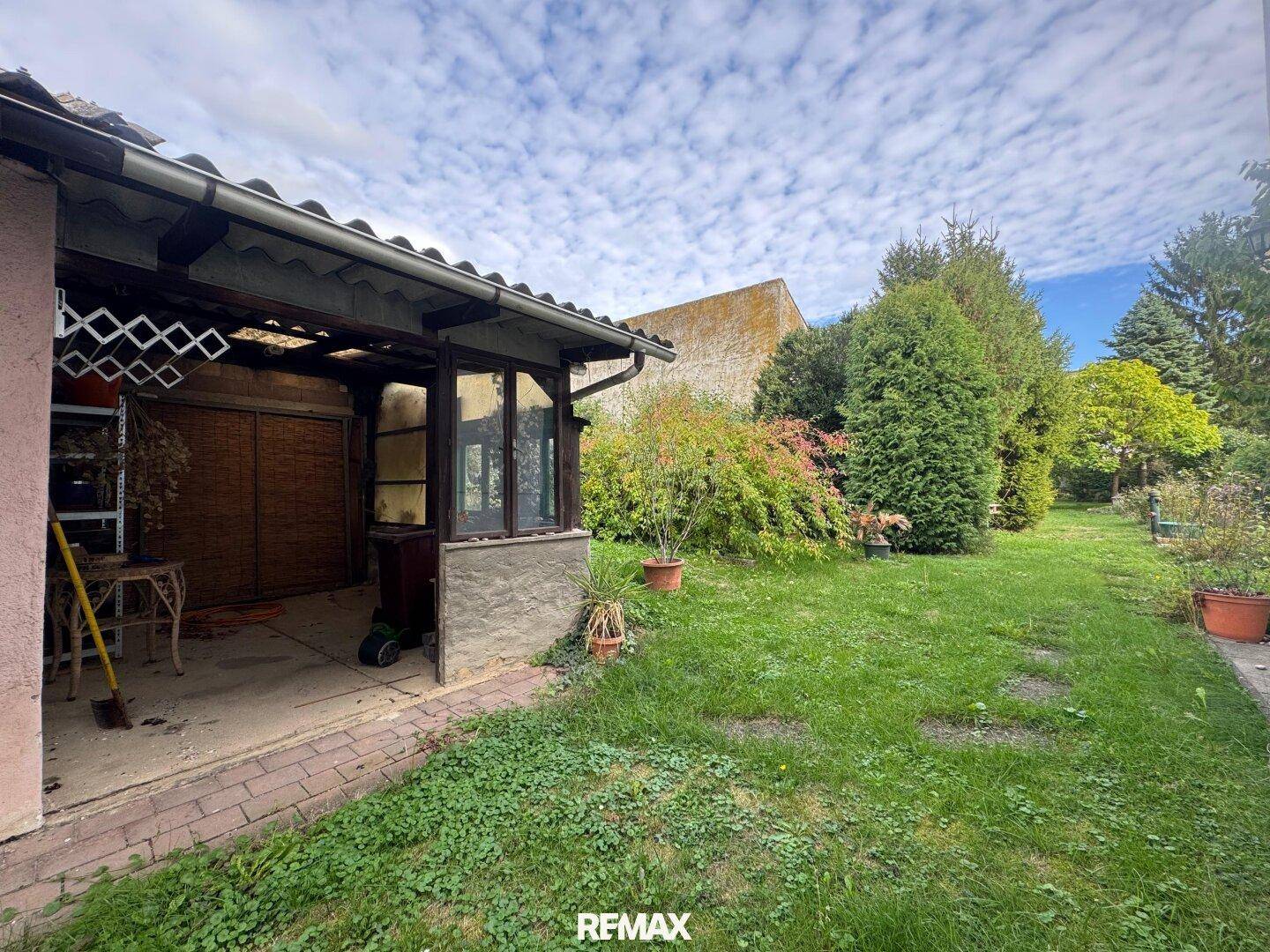 Garten mit Rasenfläche, überdachtem Bereich und Blick auf die umliegende Natur.