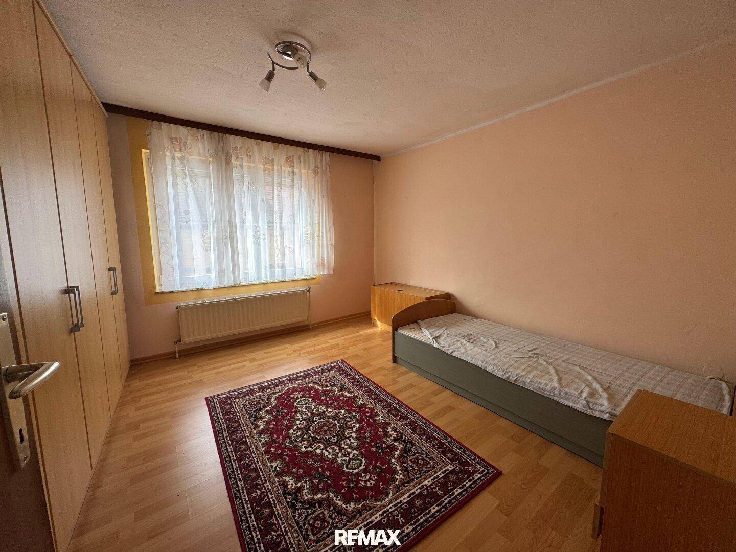 Schlafzimmer mit Laminatboden, Einbauschränken und einem Einzelbett.