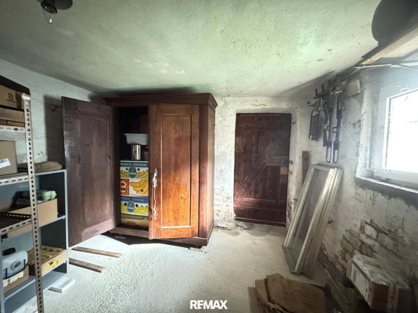 Kellerraum mit Betonboden, einem alten Holzschrank und einem kleinen Fenster, ideal als Lagerfläche.