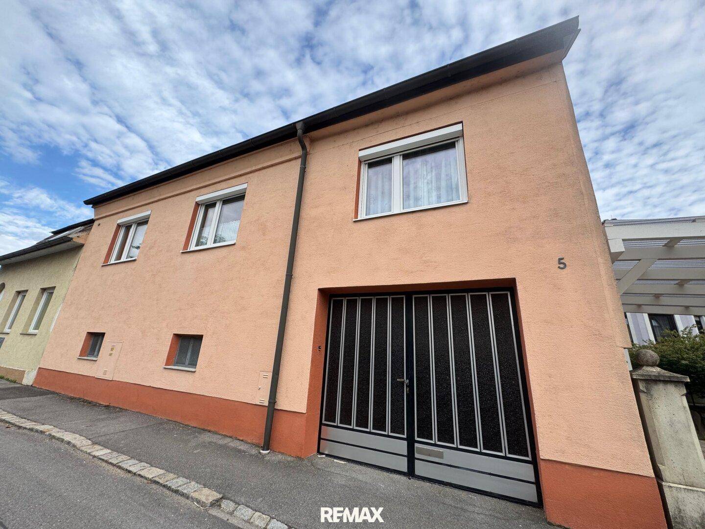 Fassade eines Hauses mit einer modernen Garagentür und mehreren Fenstern unter bewölktem Himmel.