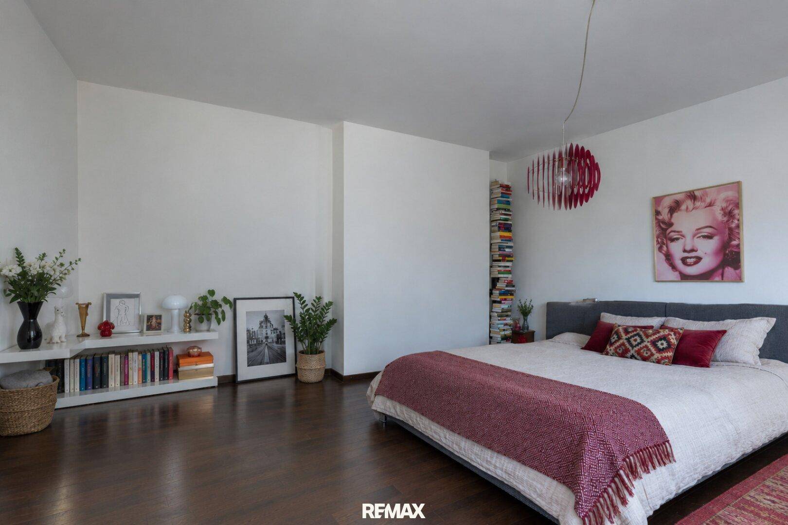 Schlafzimmer mit Holzboden, großem Bett und dekorativen Elementen wie einem Bücherregal.