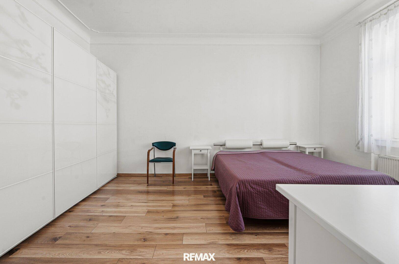 Schlafzimmer mit Holzboden, großem Kleiderschrank und einem Doppelbett mit Nachttischen.