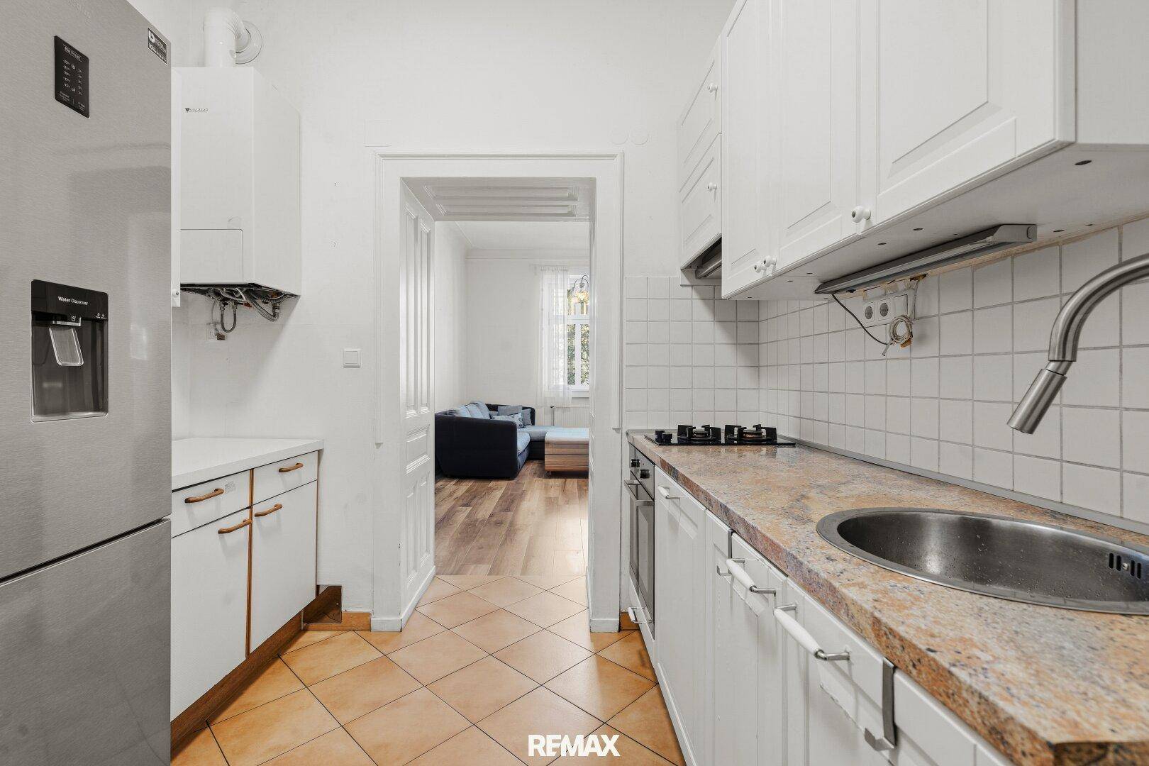Praktische Küche mit weißen Schränken, Kühlschrank und Blick in den angrenzenden Wohnbereich.