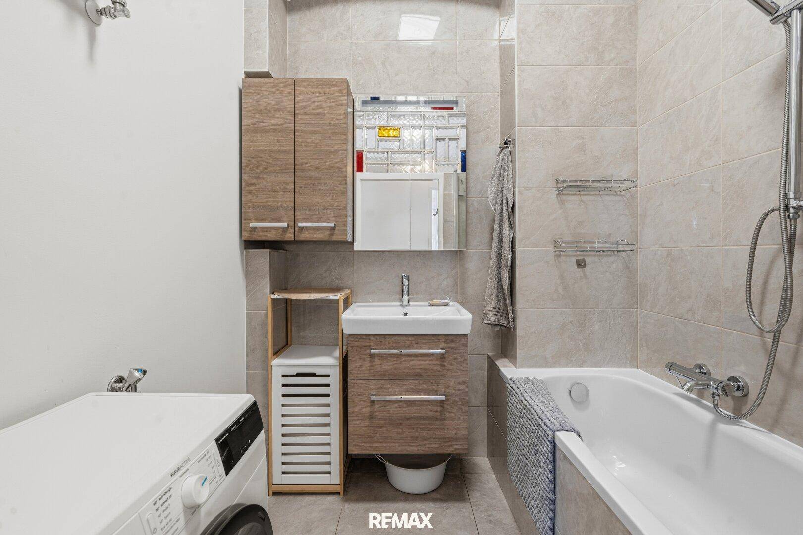 Modernes Badezimmer mit Badewanne, Waschbecken und Waschmaschine, hell gefliest.
