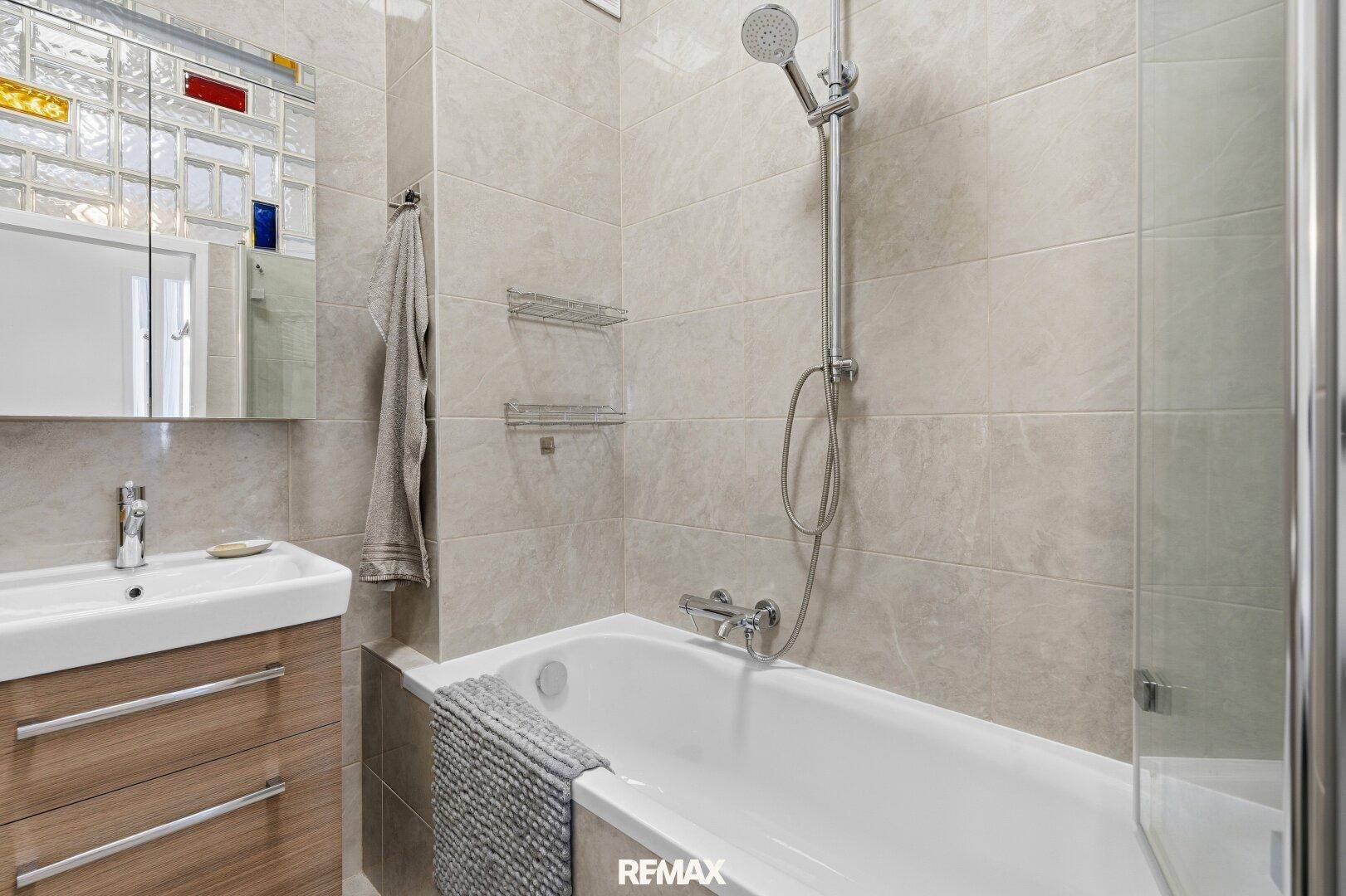 Helles Badezimmer mit Badewanne, Duschvorrichtung und modernen Fliesen, gut gepflegt.