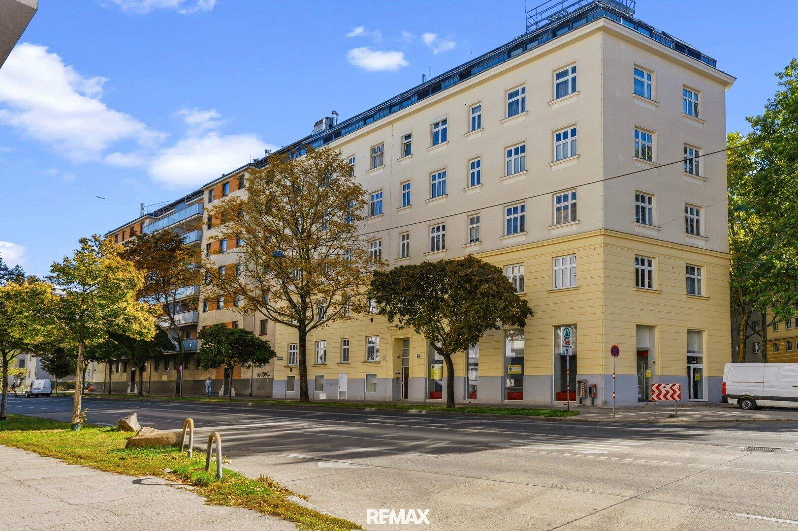 Klassisches Mehrfamilienhaus mit gelber Fassade und vielen Fenstern an einer belebten Straße.