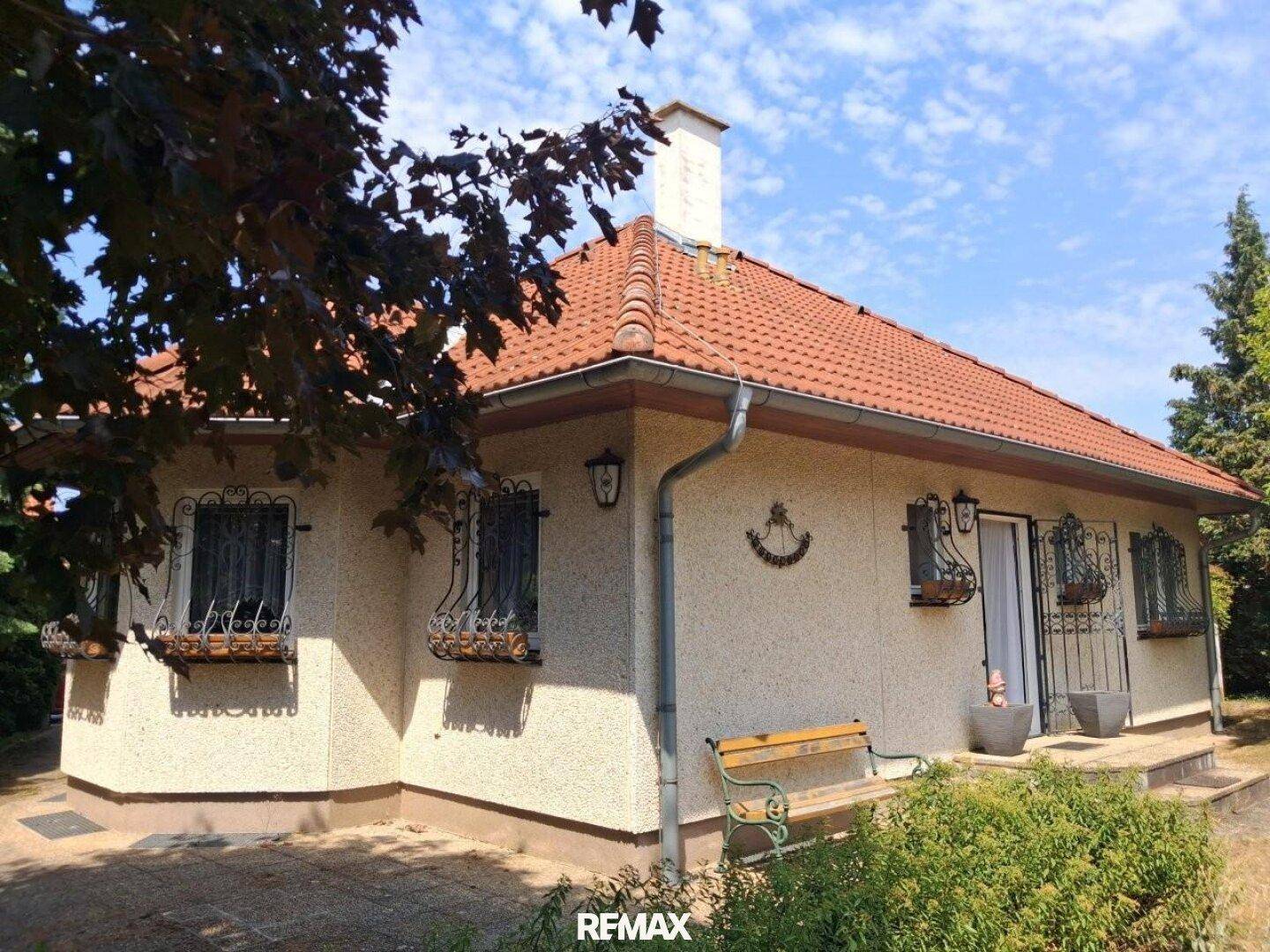 Charmantes Einfamilienhaus mit Ziegeldach und gepflegtem Vorgartenbereich unter blauem Himmel.