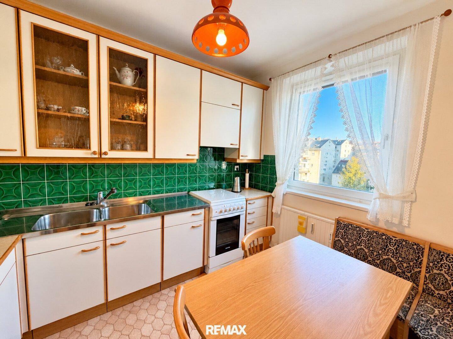 Funktionale Küche mit weißen Schränken, grünen Fliesen und einem Essbereich am Fenster.