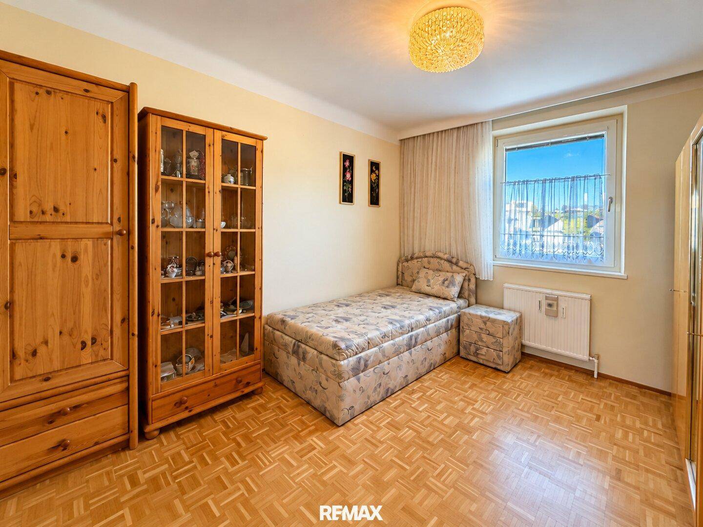 Helles Schlafzimmer mit Einzelbett, rustikalen Holzmöbeln und einem Fenster für Tageslicht.