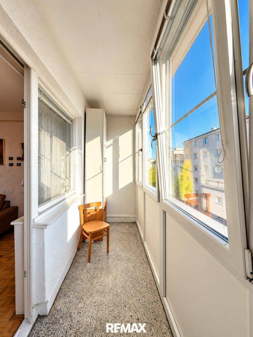 Verglaste Loggia mit sonnigem Ausblick auf die umliegenden Gebäude, ideal zum Entspannen.