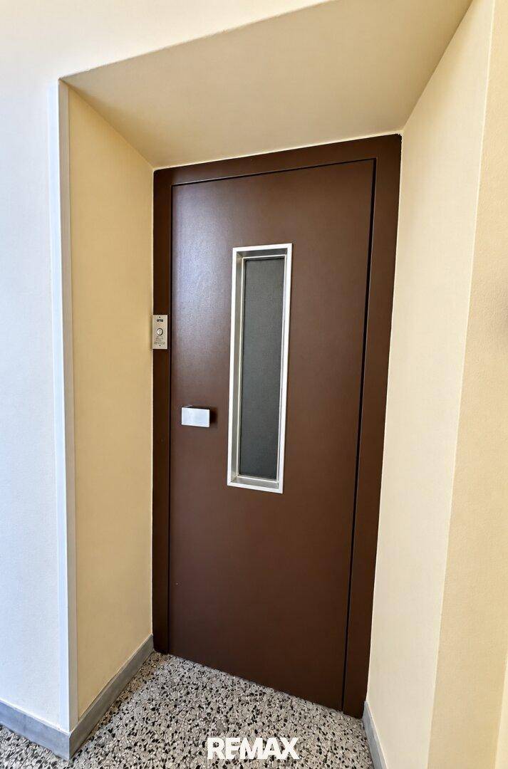 Braune Aufzugstür mit schmalem Fenster in einem Mehrfamilienhaus, bereit zur Fahrt.