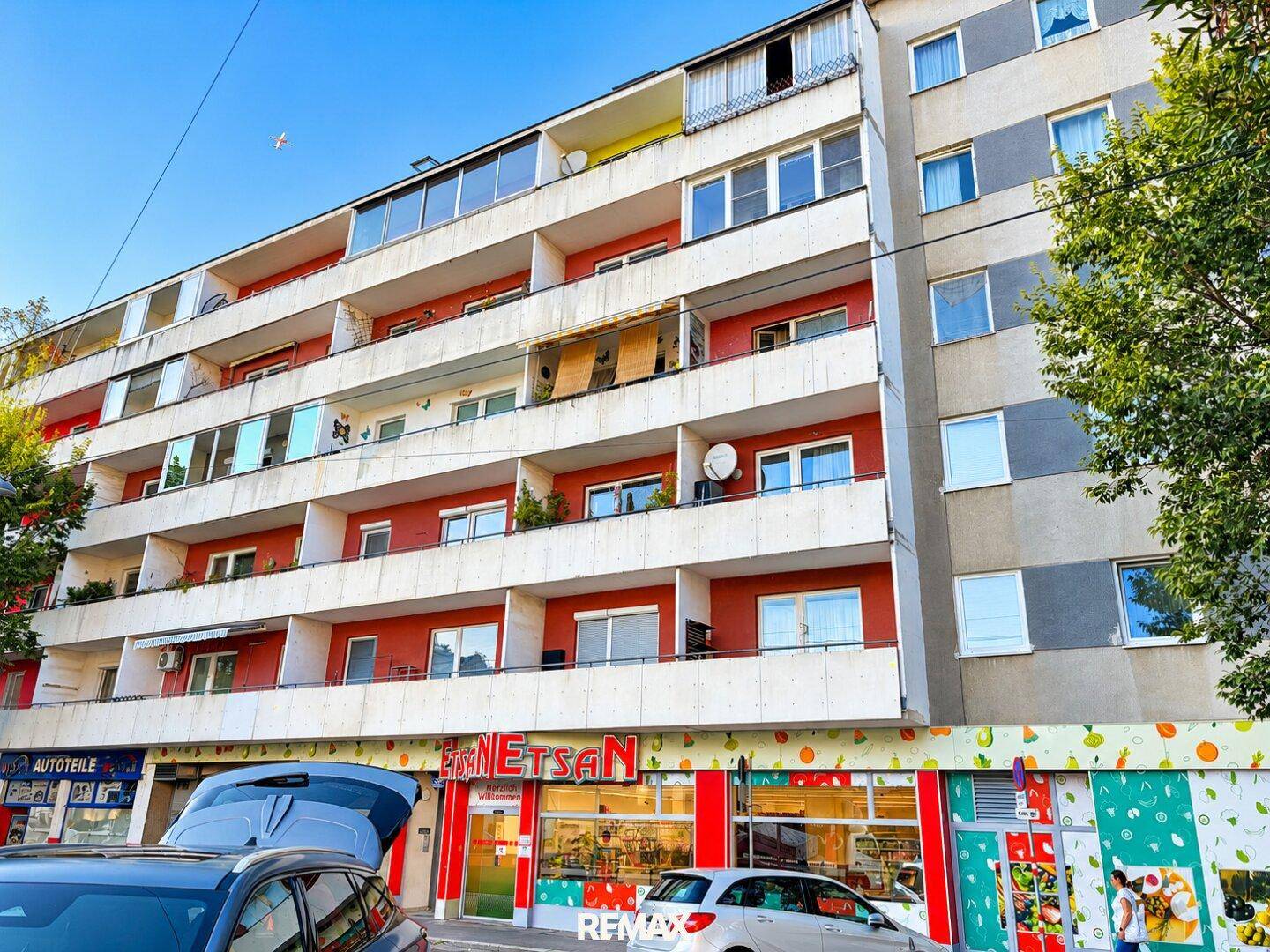 Mehrstöckiges Wohngebäude mit zahlreichen Balkonen und Geschäften im Erdgeschoss.
