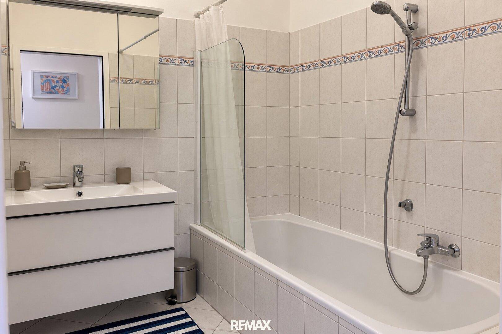 Badezimmer mit Badewanne, Duschabtrennung und hellen Fliesen an den Wänden.