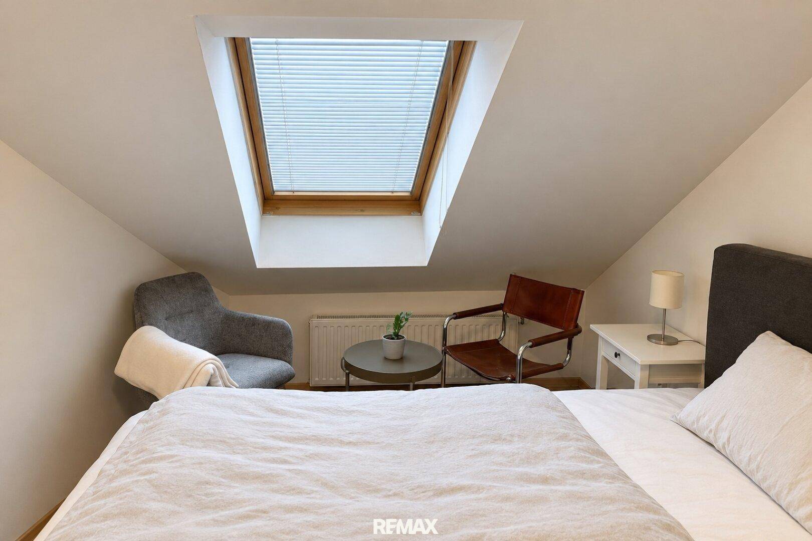 Gemütliche Ecke im Schlafzimmer mit Sessel, Beistelltisch und Dachfenster.