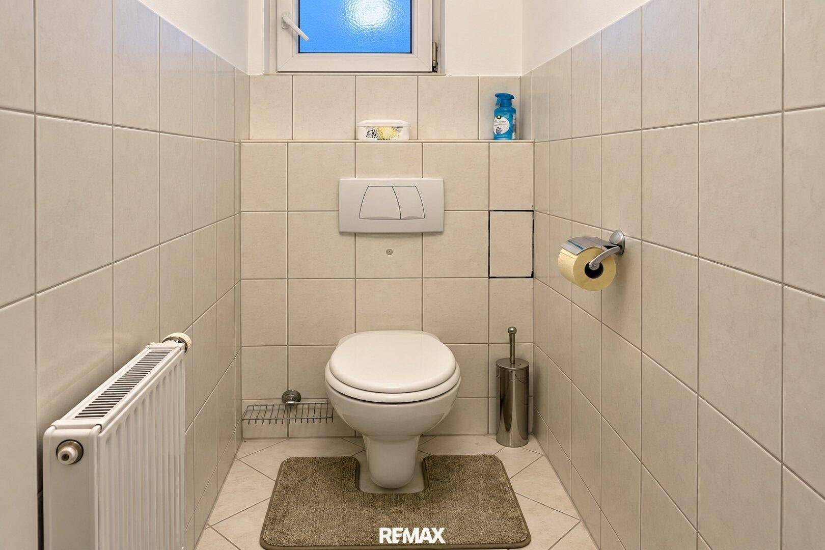 Separates WC mit wandhängender Toilette, Heizung und hellen Fliesen.