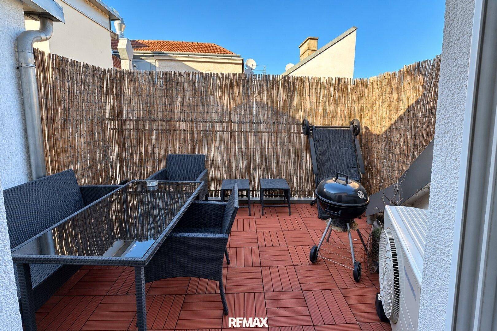 Sonniger Außenbereich mit Sitzgelegenheiten, Grill und Sichtschutz aus Bambus.