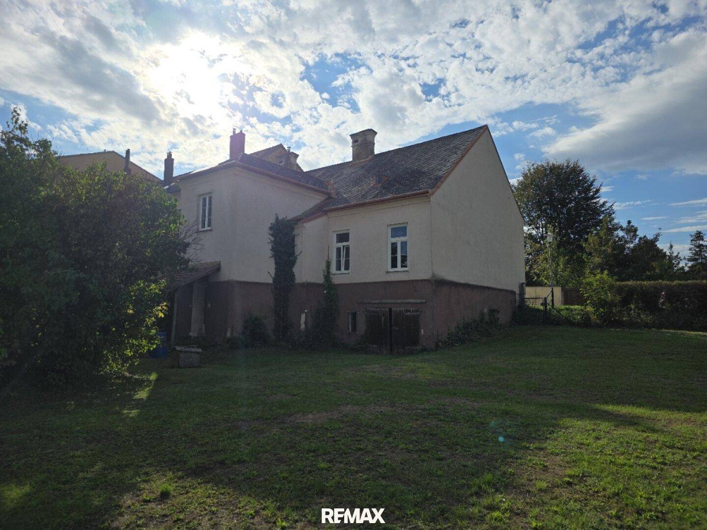 Seitenansicht des Hauses vom Garten aus, mit Blick auf die Fassade und das Dach unter sonnigem Himmel.