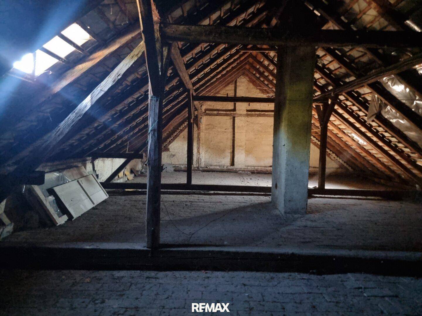 Unausgebauter Dachboden mit sichtbaren Holzbalken, Dachkonstruktion und Oberlichtern, die Licht spenden.