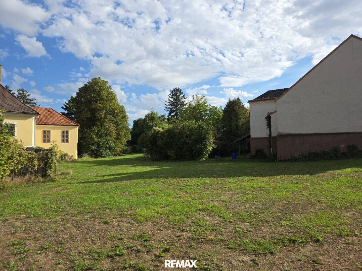 Ausgedehnte Grünfläche mit umgebenden Gebäuden und üppigem Baumbestand unter einem bewölkten Himmel.