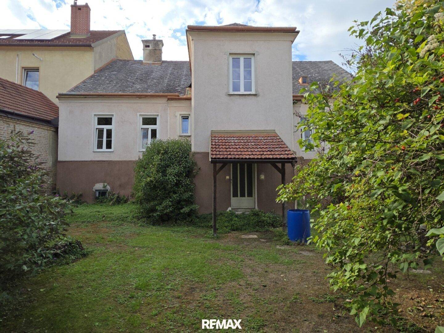 Rückansicht des Hauses mit überdachtem Eingang und einer ungepflegten Rasenfläche im Gartenbereich.
