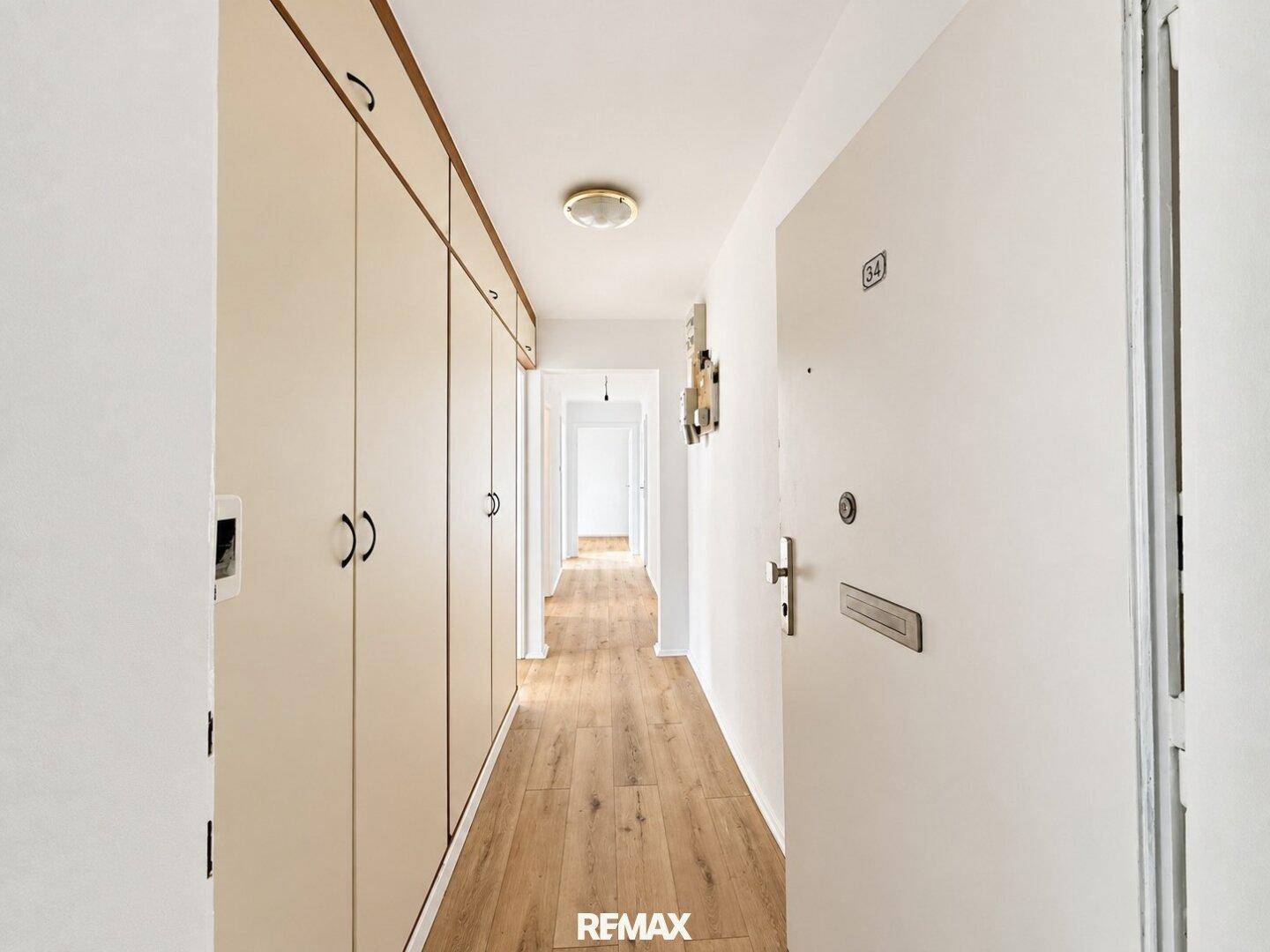 Heller Flur mit Einbauschränken, Holzboden und der Eingangstür der Wohnung.