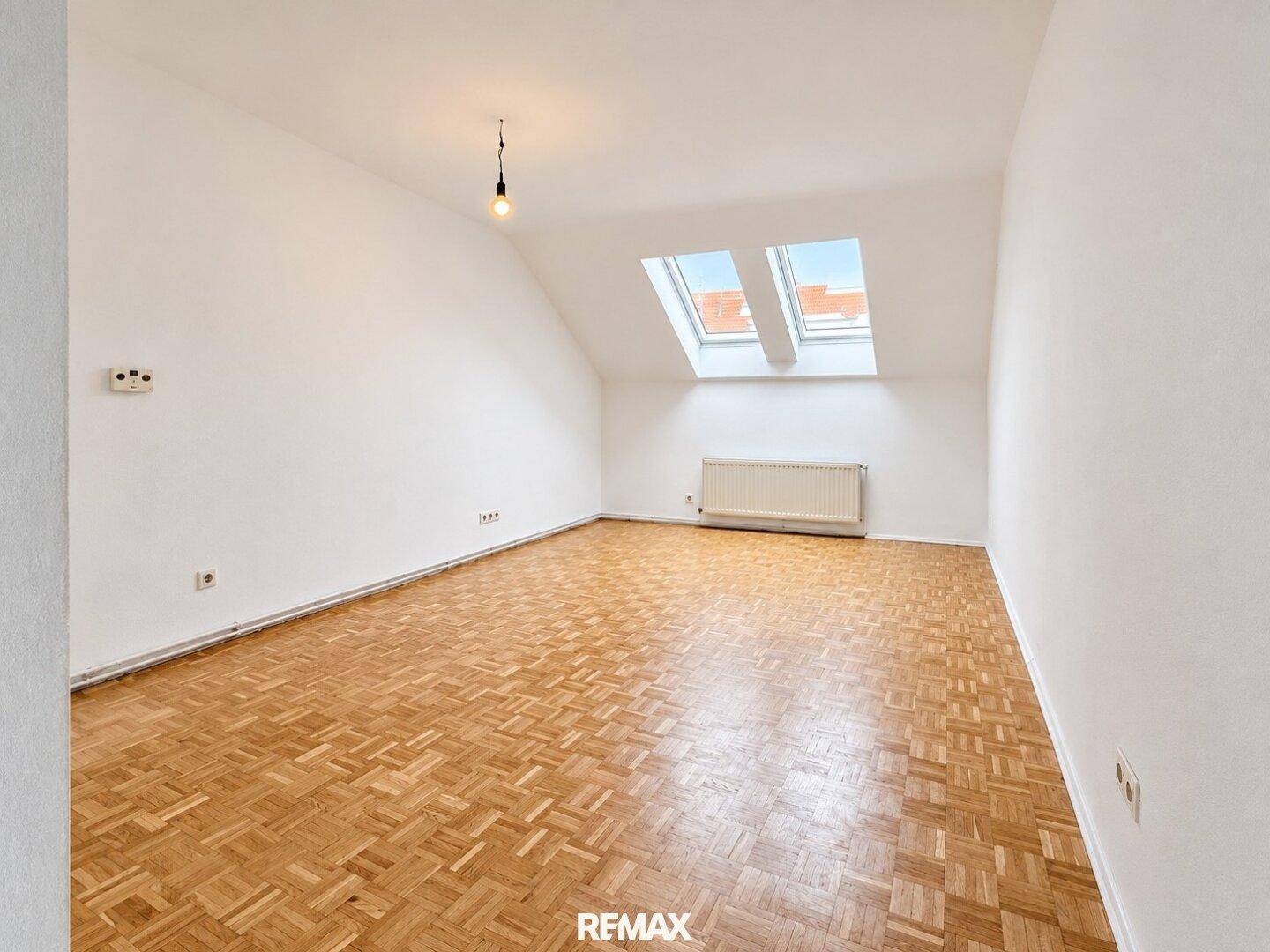 Helles Schlafzimmer mit Parkettboden, Dachschrägen und zwei Dachfenstern für Tageslicht.