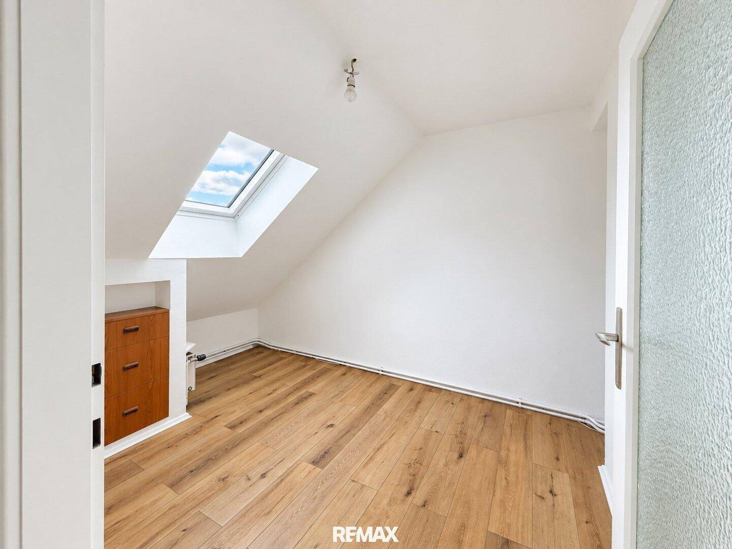 Gemütliches Zimmer mit Holzboden, Dachschräge und einem Dachfenster, inklusive Einbauschrank.