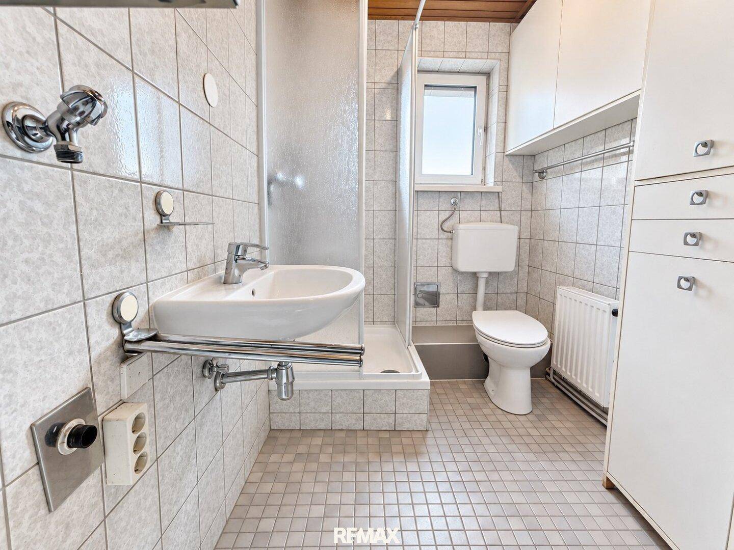 Funktionales Badezimmer mit Dusche, WC, Waschbecken und einem Fenster für natürliche Belüftung.